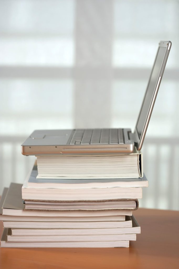 Un ordinateur portable moderne posé sur une pile de livres à l'intérieur, évoquant l'apprentissage ou le travail.